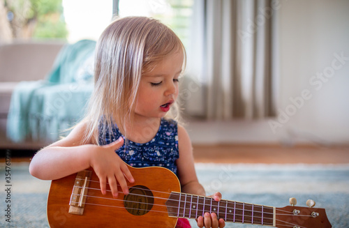 Young caucasian girl learns to play guitar or ukulele