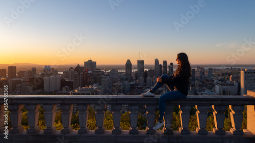 Montreal, Canada - may 2020 : young woman sitting on the Kondiaronk belvedere's stone wall and admiring the sunrise photo