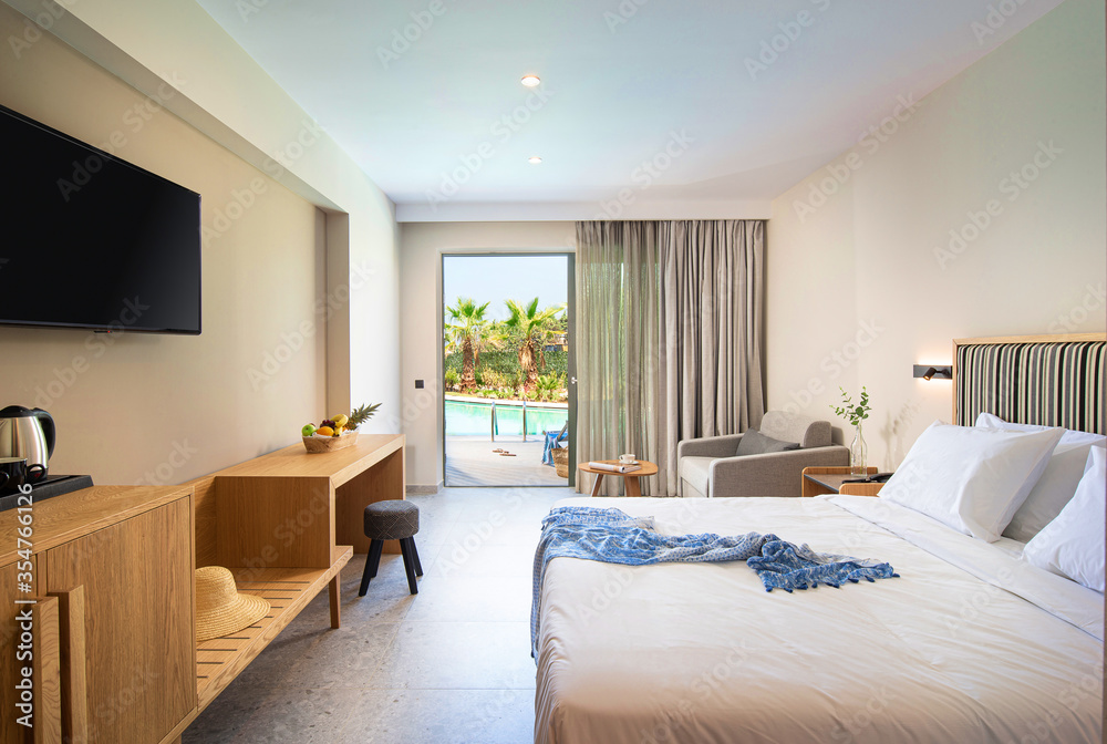 Beige striped and light wood interior of modern minimalistic style bedroom with open French window and tropic swimming pool view Beige striped and light wood interior of modern minimalistic style bedroom with open French window and tropic swimming pool view