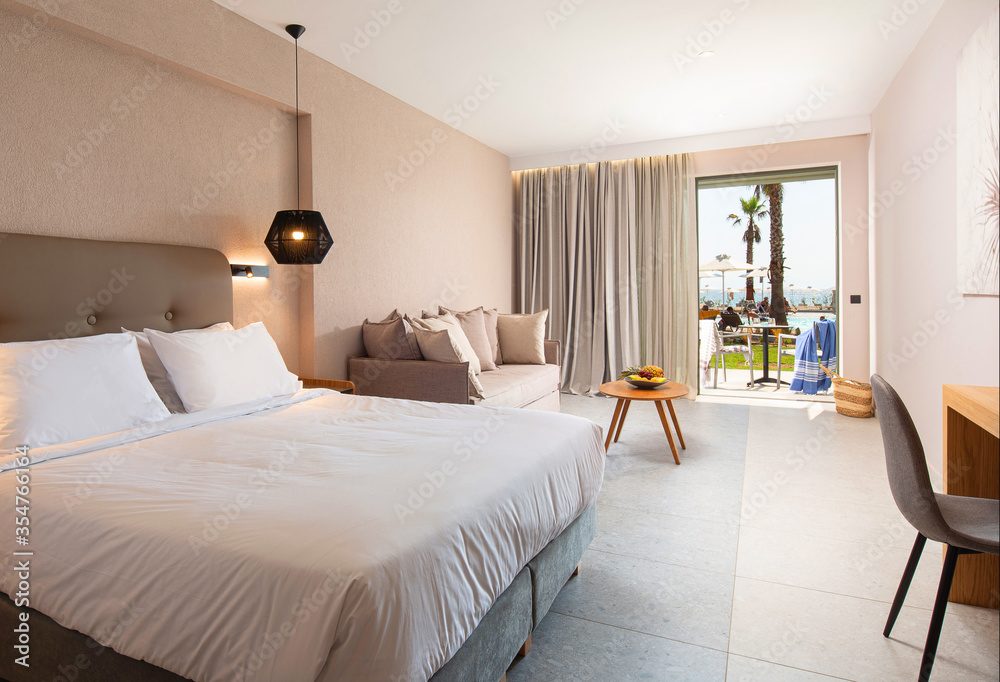 Modern design interior of hotel bedroom with soft textile furniture and open terrace with tropic swimming pool