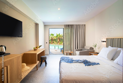 Beige striped and light wood interior of modern minimalistic style bedroom with open French window and tropic swimming pool view