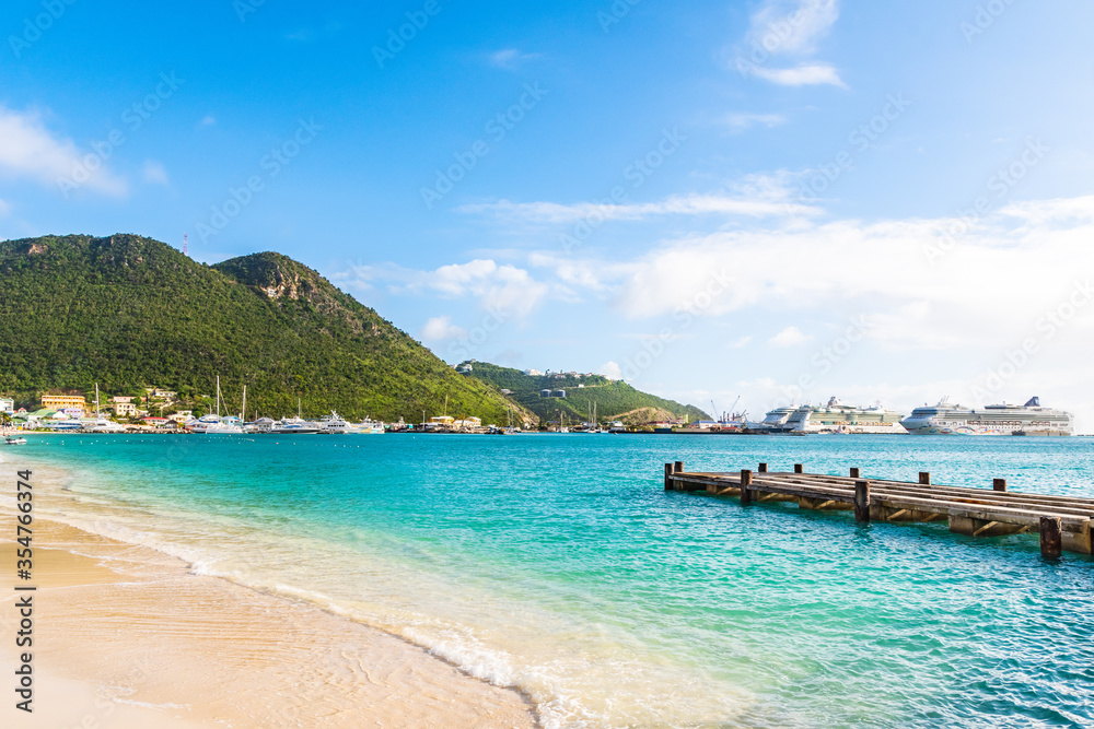Philipsburg, Sint Maarten. View from Great Bay Beach of Royal Caribbean and Norwegian Cruise Line ships docked in port near coastline mountains. Scenic tropical vacation setting.