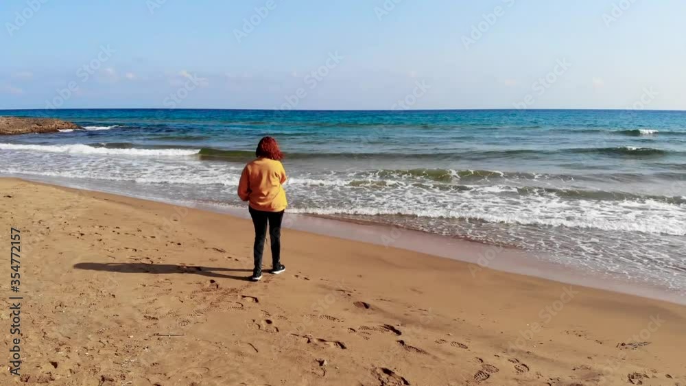 Aerial tracking shot of girl standing on beach looking at the ocean. Concept sunny winter beach. Aerial tracking shot of girl standing on beach looking at the ocean. Concept sunny winter beach.