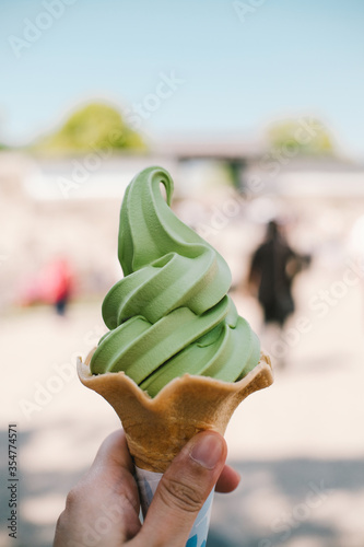Hand holding icecream cone in hot summer light nature background. Green tea icecream cone