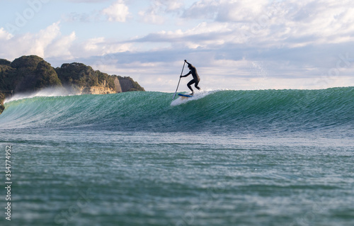 Stand Up Paddle Boarding In Japan at Sunrise and Sunset a solo rider keeping fit & healthy on the Pacific Ocean in a black wetsuit, also catching some large waves, The ocean is blue with a nice sky. photo