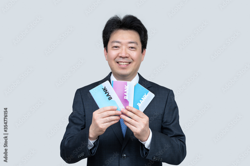 A middle-aged Asian businessman holding a bank passbook in his hand on a gray background. A middle-aged Asian businessman holding a bank passbook in his hand on a gray background.