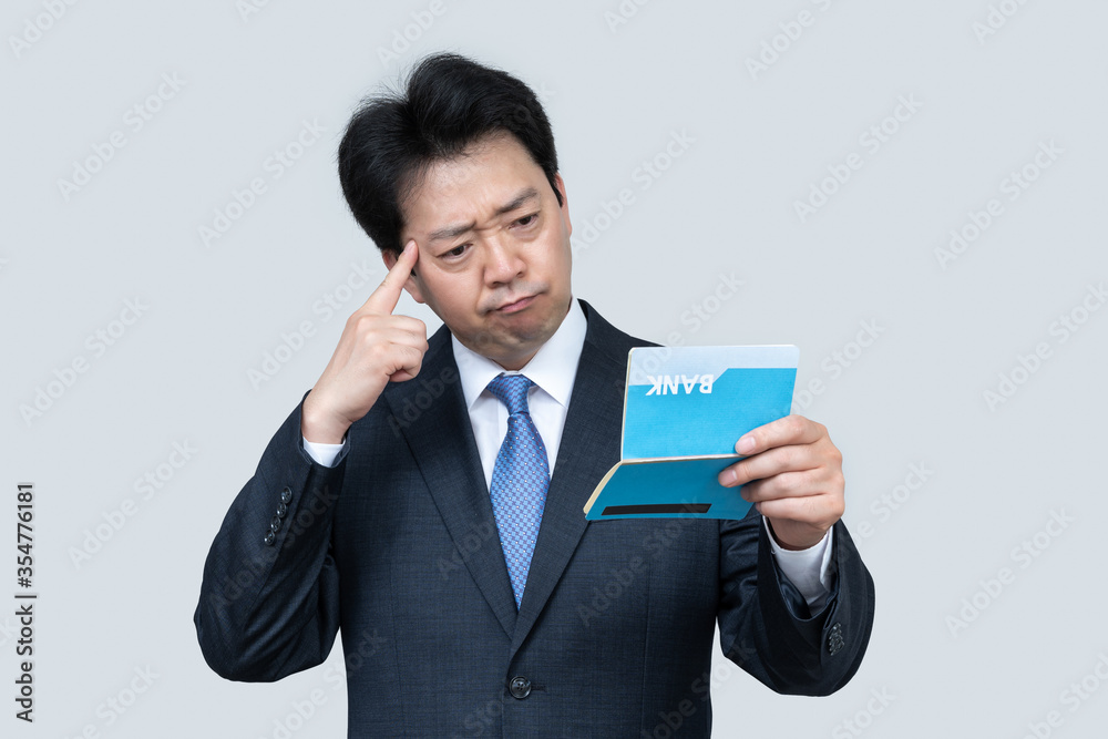 A middle-aged Asian businessman holding a bank passbook in his hand on a gray background. A middle-aged Asian businessman holding a bank passbook in his hand on a gray background.
