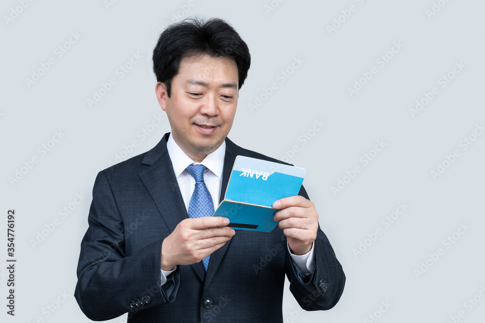 A middle-aged Asian businessman holding a bank passbook in his hand on a gray background. A middle-aged Asian businessman holding a bank passbook in his hand on a gray background.