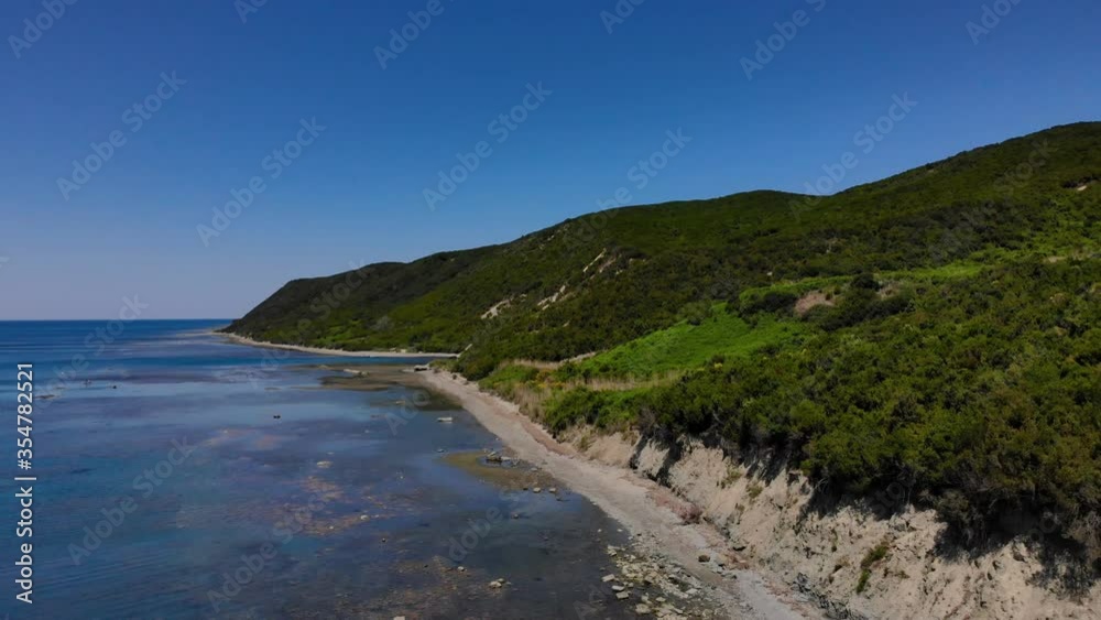 Sea scenery with calm water on rocky shore of Mediterranean bordered by green hills on a bright blue sky background Sea scenery with calm water on rocky shore of Mediterranean bordered by green hills on a bright blue sky background