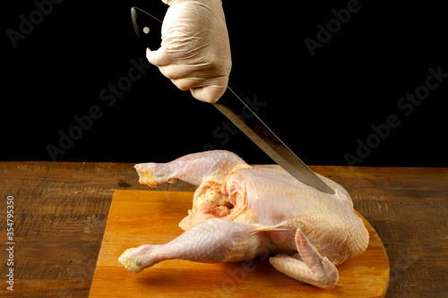 Woman cuts chicken carcass with a knife on a wooden board.