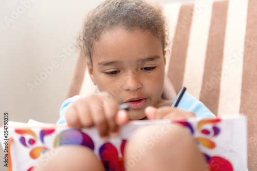 Little girl drawing at home sitting on chair.