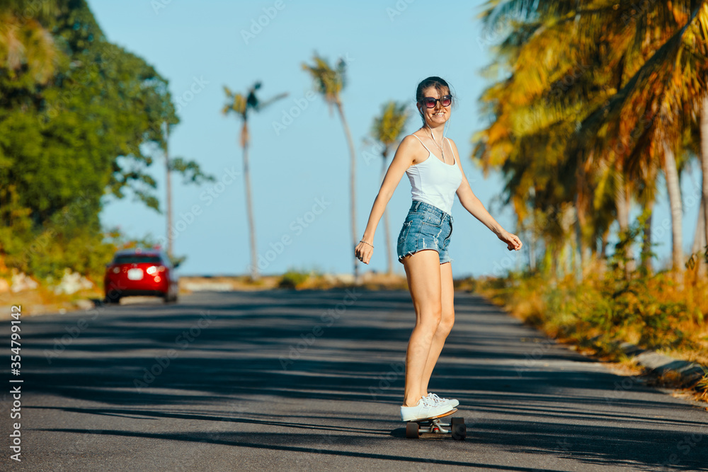 Outdoor summer portrait of cheerful young woman riding longboard in sunny weather