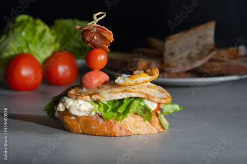 open sandwich with cheese, vegetables, meat and quail egg with out of focus bread slices and vegetables