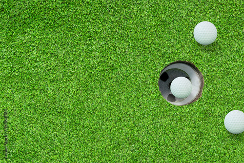 Top view one of white golf balls in hole on green grass meadow field.