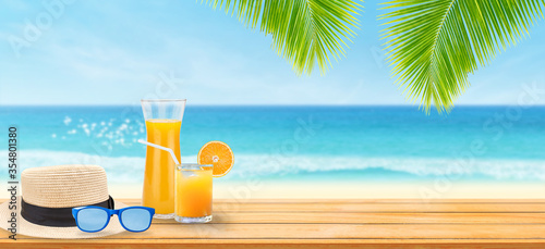 Summer Vacation Concept : Welcome drink orange juice punch, weave hat and sunglasses put on wooden table with blurry image of blue water and seascape view in background.