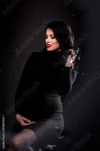 Portrait of beautiful pregnant girl in a black bodie on a black background. VOGUE style. amily and maternity. Close up