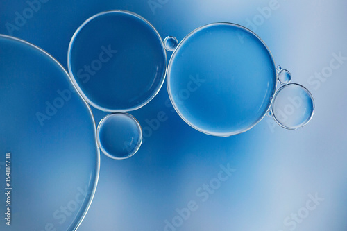 Macro of oil and water bubbles creating a scientific image of cell and cell membrane with a blue and white gradient and in a horizontal format.