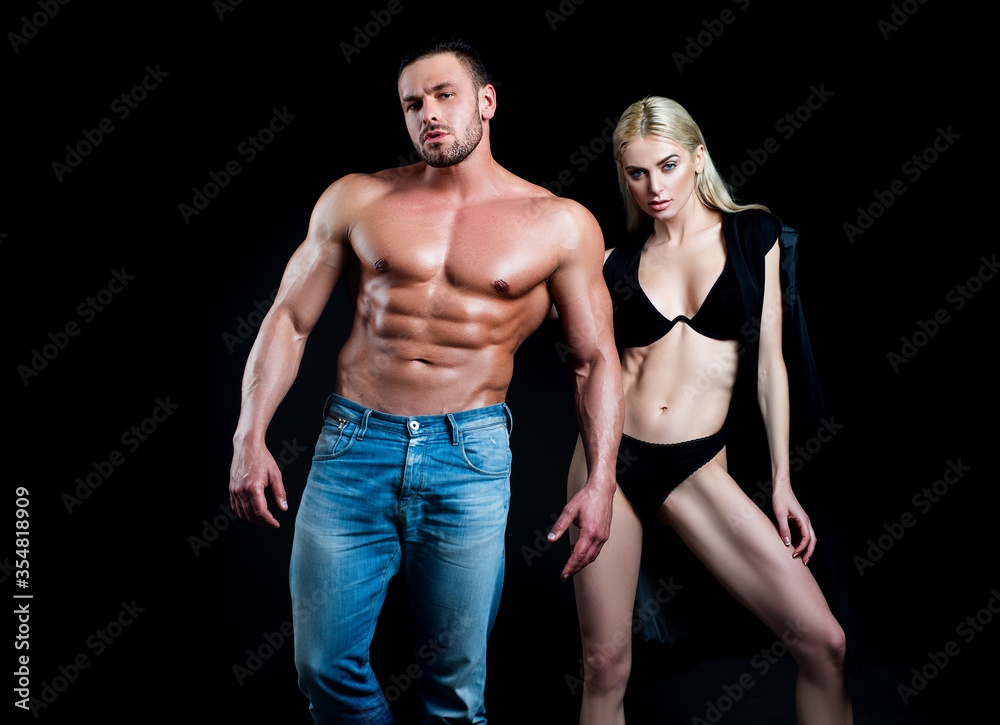 Fitness couple over black background. Fit fashion couple posing. Beautiful sexy couple in love dressed in blue jeans. Passionate couple in studio.