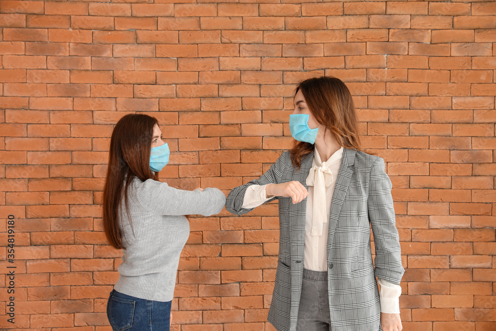 Young women greeting each other near brick wall. Concept of social distance during coronavirus epidemic Young women greeting each other near brick wall. Concept of social distance during coronavirus epidemic