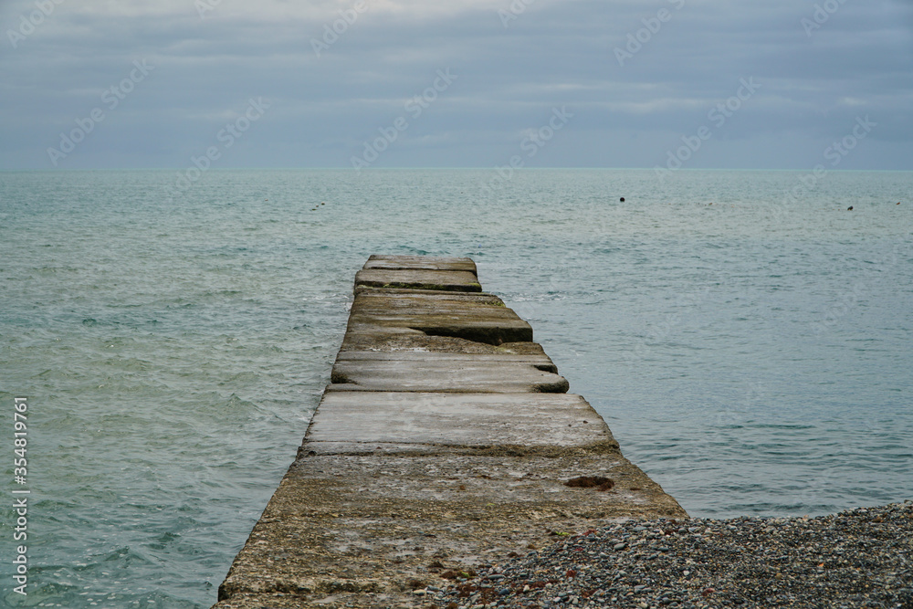 Wooden pier on the beach. Sunset and calm ocean. Calm. Stone beach of the gray cold sea. High quality photo