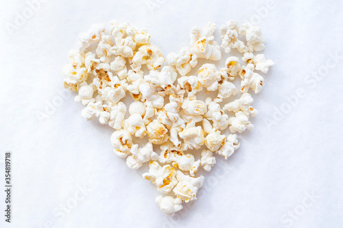 Tasty salted popcorn in shape of heart on white background. Top view minimalistic popcorn