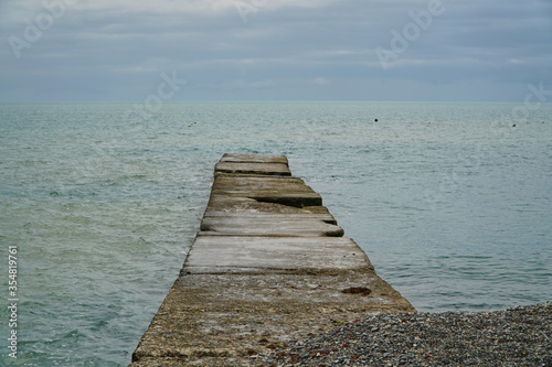 Wooden pier on the beach. Sunset and calm ocean. Calm. Stone beach of the gray cold sea. High quality photo