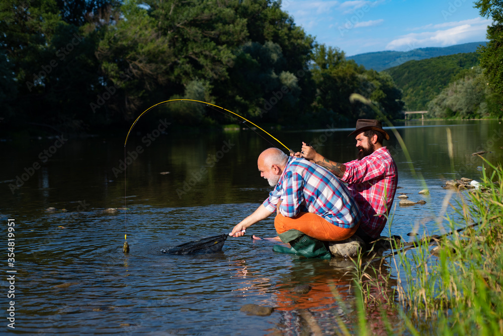 Angler catching the fish. Senior man fishing. Bearded brutal hipsters fishing. Men relaxing nature background. Against the background of the water with a reflection of the forest. Fishing. Angler catching the fish. Senior man fishing. Bearded brutal hipsters fishing. Men relaxing nature background. Against the background of the water with a reflection of the forest. Fishing.