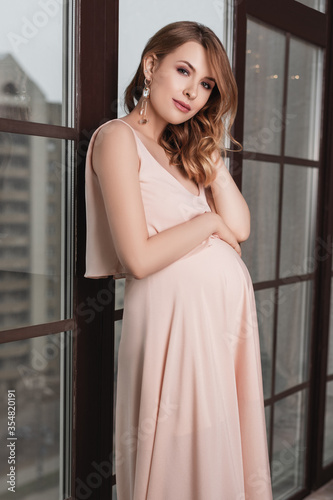 Pregnant woman in dress holds hands on belly.Fashion portrait of happy pregnant woman.Pregnancy, maternity, preparation and expectation concept. Close-up, copy space. 