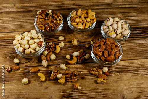 Assortment of nuts on wooden table. Almond, hazelnut, pistachio, walnut and cashew in glass bowls. Healthy eating concept
