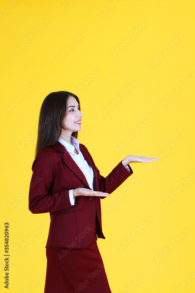 Smart Caucasian woman in red suit smiling and her hand open for present isolated on yellow background. Smart Caucasian woman in red suit smiling and her hand open for present isolated on yellow background.