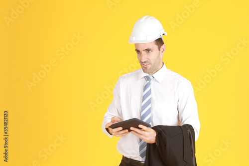 Handsome and smart engineer in suit and white shirt and Wearing a white safety engineer hat with hand holding smartphone isolated on yellow background. Copy Space