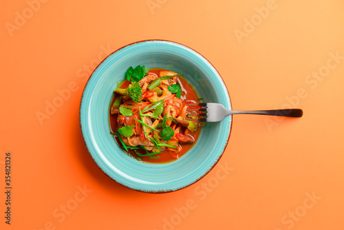Meat salad with vegetable and fresh greenery served in a bowl isolated on bright orange background.