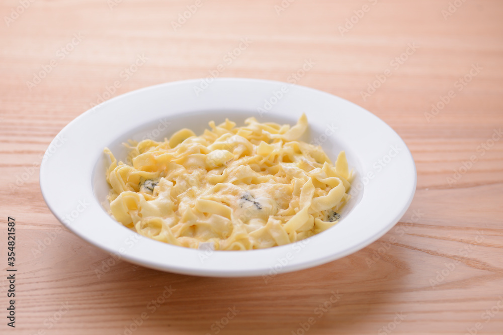 Pasta with mushrooms in a creamy sauce served in white plate on light wooden table.