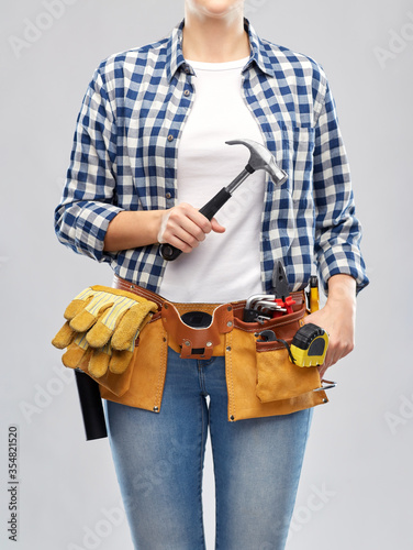 repair, construction and building concept - woman or builder with hammer and working tools on belt over grey background