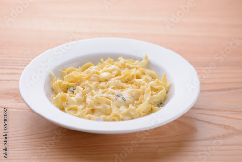 Pasta with mushrooms in a creamy sauce served in white plate on light wooden table.