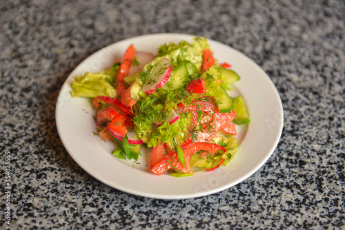 Vegetable salad with radishes,cucumber, sweet pepper and dill. Served in a white plate over grey textured table.