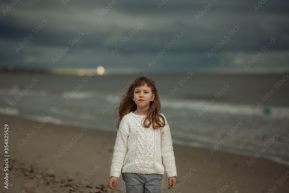 
girl in a warm sweater walks along the coast in cloudy weather towards the wind