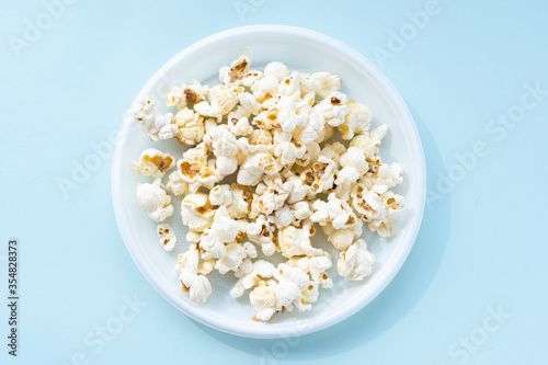 Tasty salted popcorn in plastic bowl on blue background. Cinema and entertainment concept. Close up, top view and shooting in studio.
