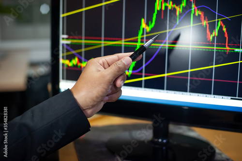 Businessman Trader hand point pen on chart trading screen to analyze market trends