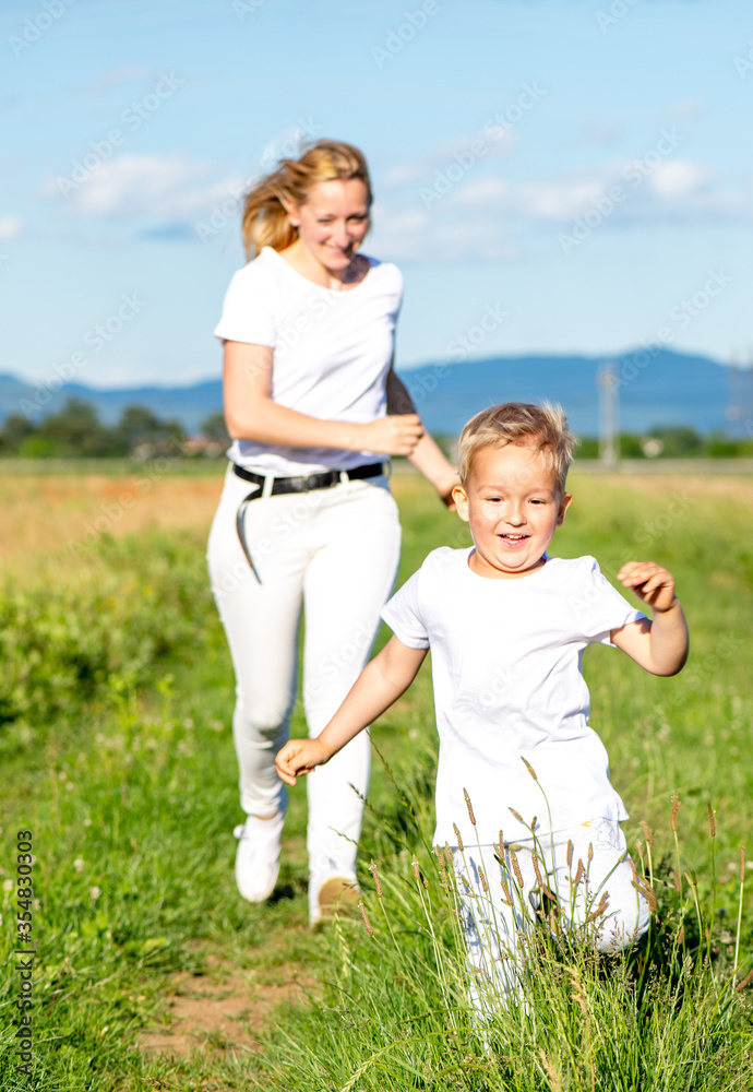 Mom and son are running, holding hands across the field in white T-shirts, vertical photo Mom and son are running, holding hands across the field in white T-shirts, vertical photo