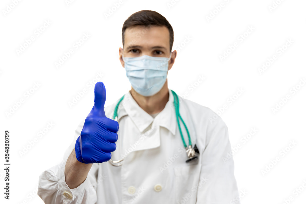Young doctor with stethoscope in protective mask and gloves showing thumbs up sign isolated on white background. Focus on hand. Young doctor with stethoscope in protective mask and gloves showing thumbs up sign isolated on white background. Focus on hand.