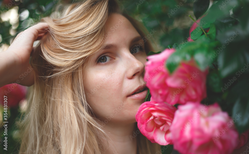 Fototapeta premium blond woman smiling in a flowering bush of pink roses