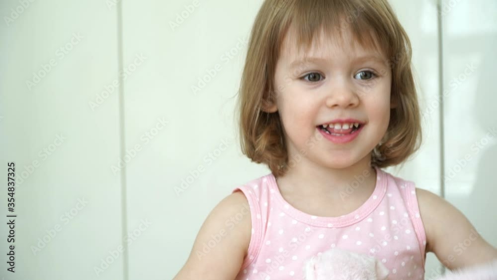 Portrait of little cute funny 3 year old girl looks at camera, smiles and laughs. Happy child plays with pink teddy bear. Close up Portrait of little cute funny 3 year old girl looks at camera, smiles and laughs. Happy child plays with pink teddy bear. Close up