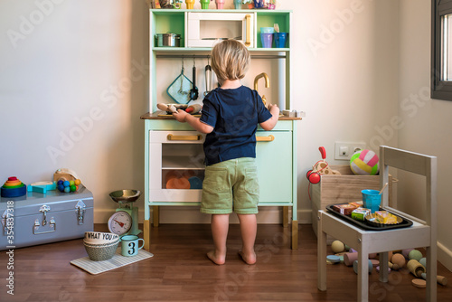 Little blond boys play with a toy kitchen at home during quarantine. Fun at home.