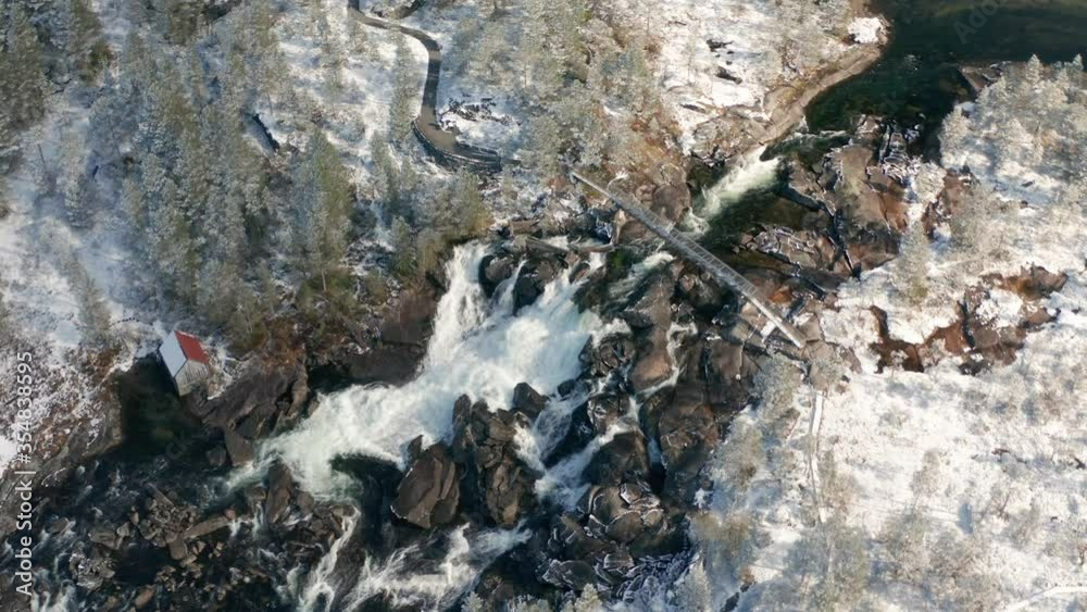 Aerial view of the Likholefossen waterfall on Gaula river in Norway. A turbulent mass of water rushing down in the narrow rocky channel. A narrow steel bridge hangs above the waterfall. Aerial view of the Likholefossen waterfall on Gaula river in Norway. A turbulent mass of water rushing down in the narrow rocky channel. A narrow steel bridge hangs above the waterfall.