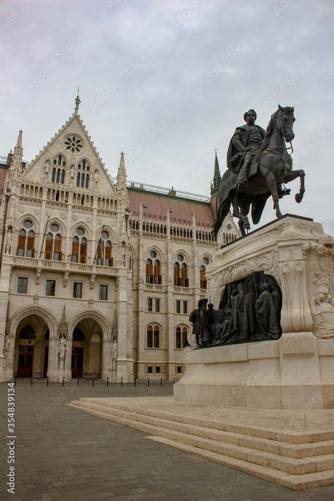 Landscape view of Hungarian Parliament Building (Országház) with statue on the Danube during cloudy and rainy day