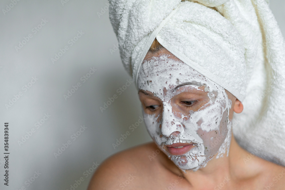 Fototapeta premium Shy woman on a white background clean face cream on face towel in hair on head.