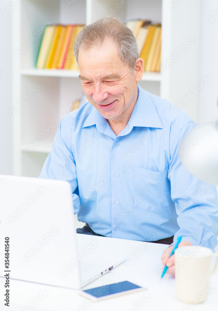 Fototapeta premium Handsome elderly man with a smile works at the computer in the office