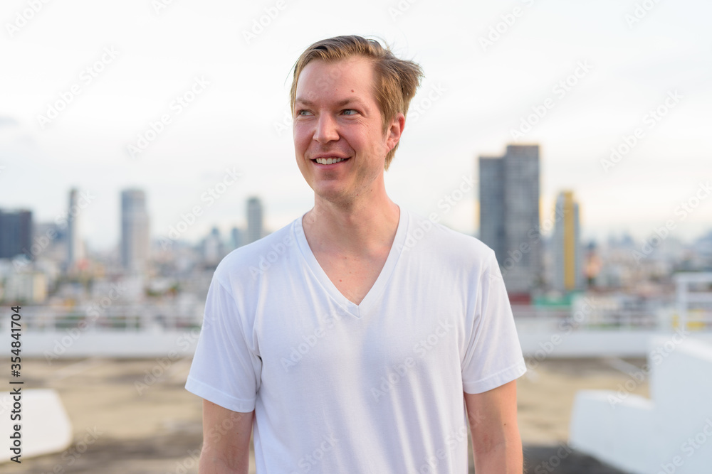 Happy young handsome man with blond hair thinking against view of the city Happy young handsome man with blond hair thinking against view of the city