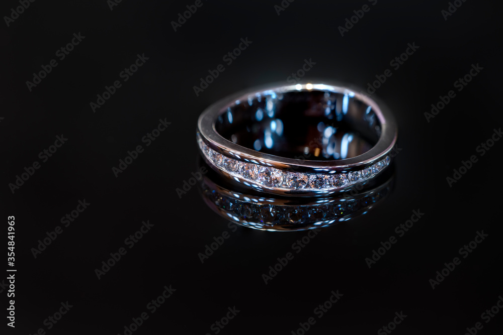 Women's wedding ring made of white gold with zircons on a shiny black background. Women's wedding ring made of white gold with zircons on a shiny black background.